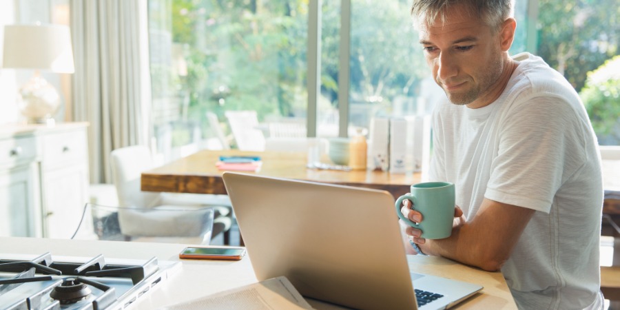 man sitting and holding a cup while read laptop