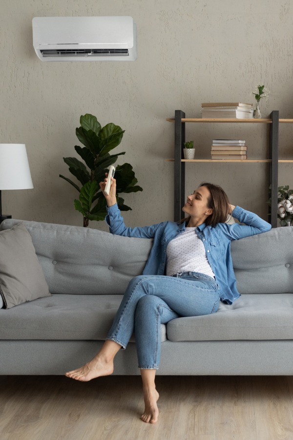 woman sitting on sofa looking comfortable with ductless unit on wall above her